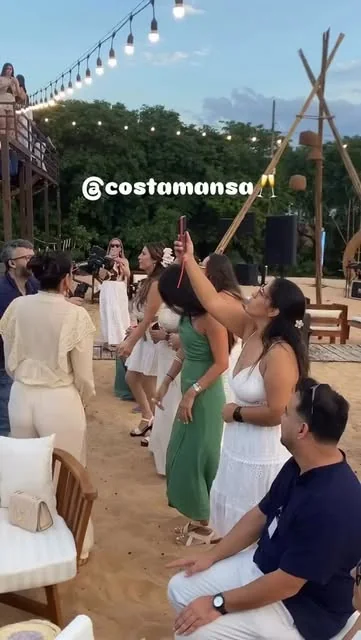 Grupo brindando bajo guirnaldas de luces sobre la arena de CostaMansa